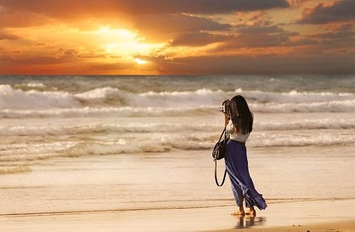 Woman Taking a Picture on the Beach at Sunset